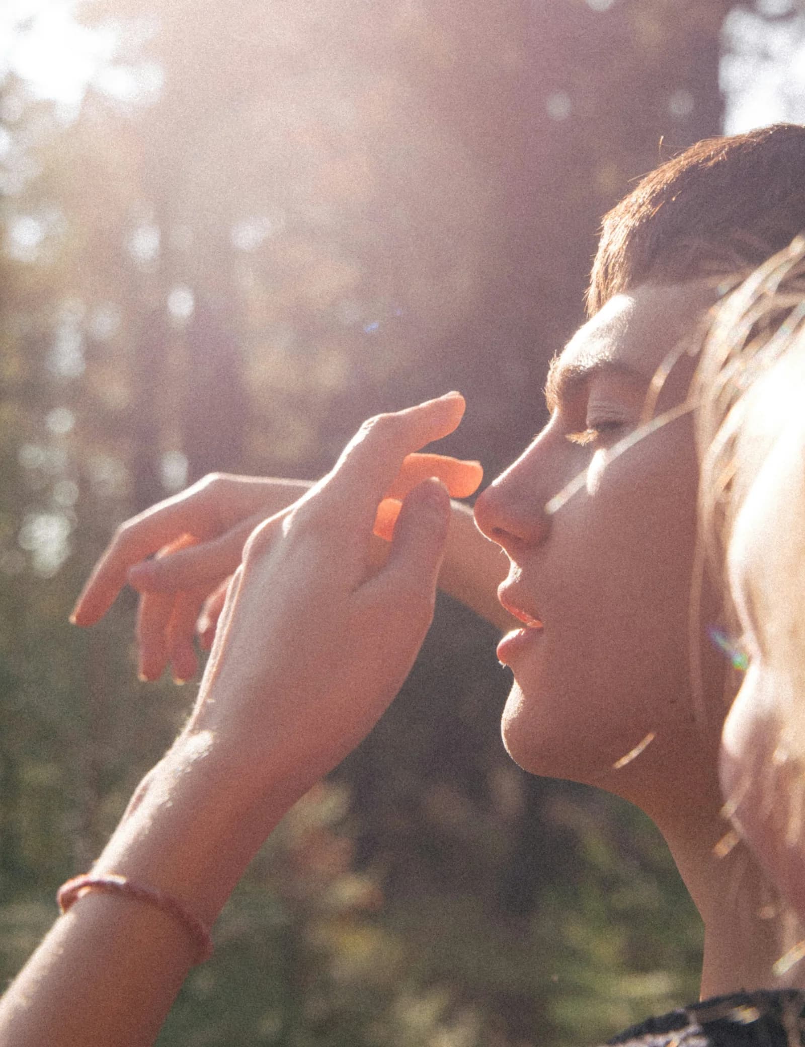 A woman in profile with her hand raised in soft woodland sunlight