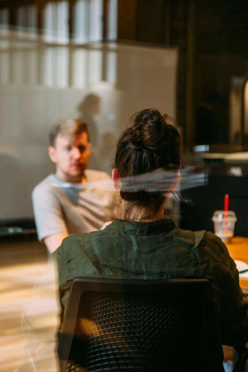 Two people in conversation at a table, seen through glass