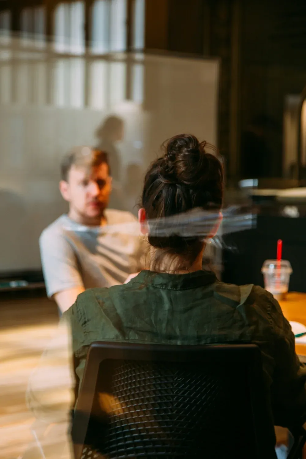 Two people in conversation at a table, seen through glass