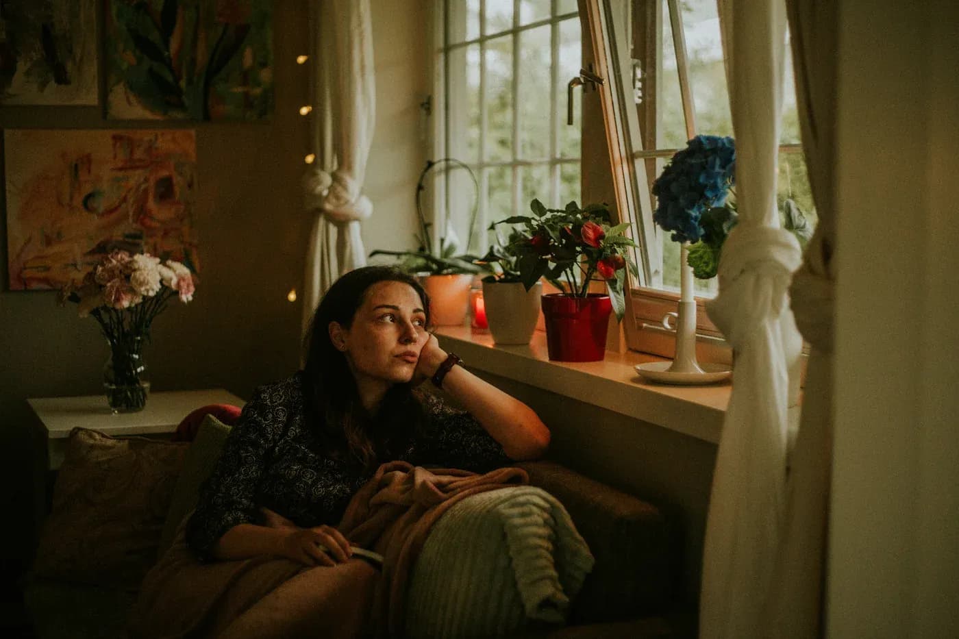 A person sitting on a sofa looking towards a window surrounded by plants